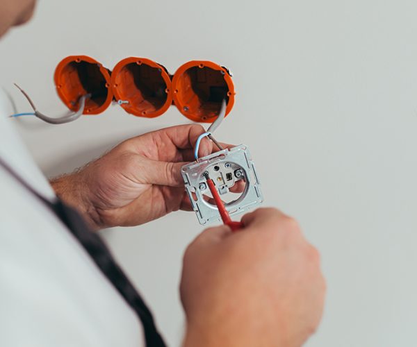 Male worker professional electrician mounts an electrical outlet in the apartment after repair, close-up photo of the installer